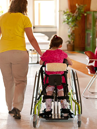 A physical therapist at a school helps guide a child in a gait trainer through the classroom