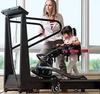A young girl with special needs uses the treadmill to practice gait training helped by her therapist
