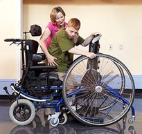 A teacher helps a student in the classroom transition from adaptive standing equipment to a chair