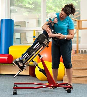 A young boy is assisted by his therapist in a medically necessary stander