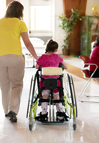 A teacher walks through the classroom with a student in a special needs standing device 