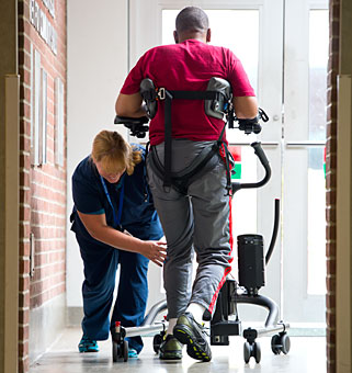 A therapist helps guide a client down a hallway to practice ambulation and gait training in a Rifton TRAM