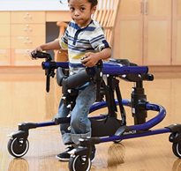 A young boy walks in the new Rifton Pacer gait trainer shown in blue with the multi-positioning saddle reversed to make it a posterior walker.