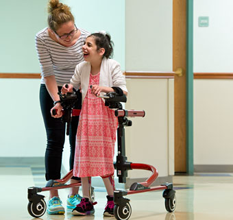 A therapist assists a young girl smiling as she practices gait training