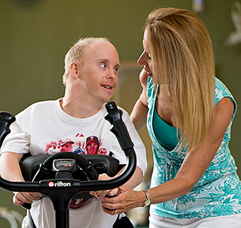 A man smiles at his therapist while walking in the Rifton TRAM.