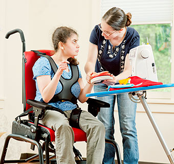 A therapist helps a student with disabilities use an adaptive sewing machine as part of the school-based transitional services program.