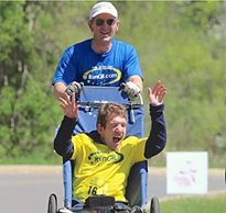 Johnny Agar cheers as he is pushed in an all-terrain stroller by his dad while training for the Kona Ironman.