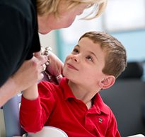 A child with special needs wearing a red shirt smiles as he looks at his therapist while positioned in a Rifton Hygiene and Toileting System.