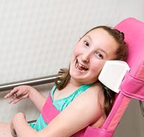 A young girl smiles happily while wearing her swimsuit as she reclines in the Rifton Wave bath chair.