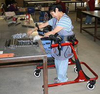 A woman with disabilities stands in a red Pacer gait trainer to access her vocational work in a sheltered workshop.