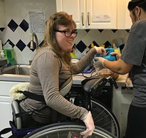A young woman uses adaptive equipment for standing skills as she works in the kitchen.