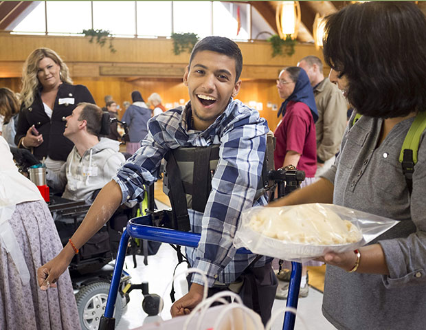 A young man in a blue rifton pacer, smiles as he looks at the apple pie he made during rifton's birthday party.