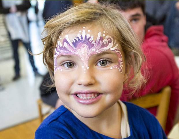 A girl with her face painting on her forehead smiles for the camera at rifton's birthday celebration.