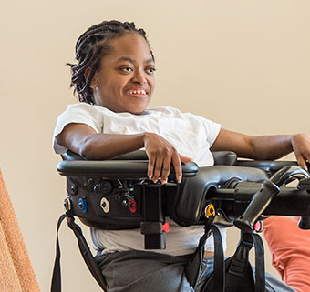 A young woman smiles as she is positioned for seat to seat transfer in the Rifton TRAM.