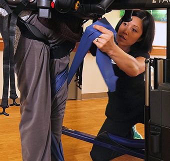 A physical therapist wraps a Theraband around the leg of a client in a Rifton E-Pacer to assist with unweighted gait training.