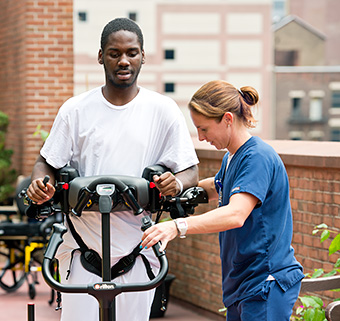 A young physical therapist guides the walking of a TBI patient in a Rifton TRAM.
