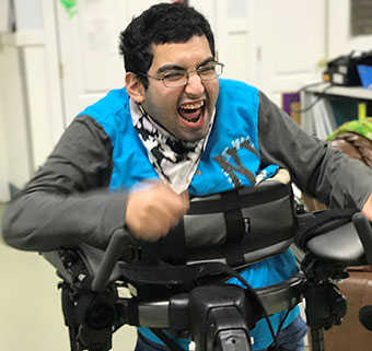 A teenage boy using a gray Rifton Pacer gait trainer to walk.