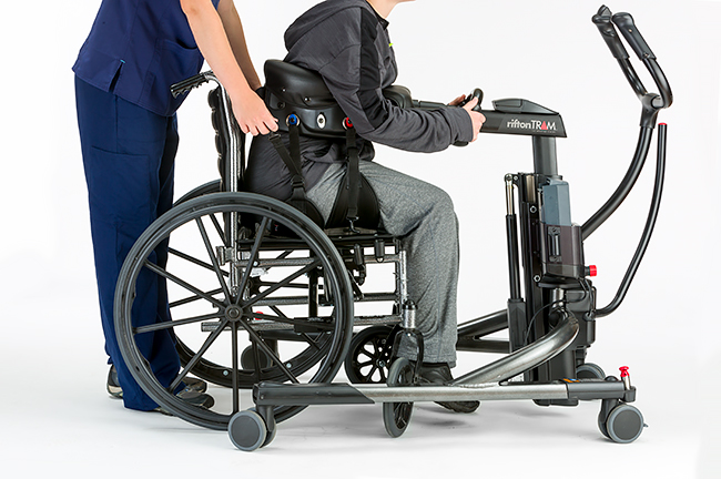 A caregiver adjusts the straps of a Rifton TRAM to prepare for a transfer of a client sitting in a wheelchair.