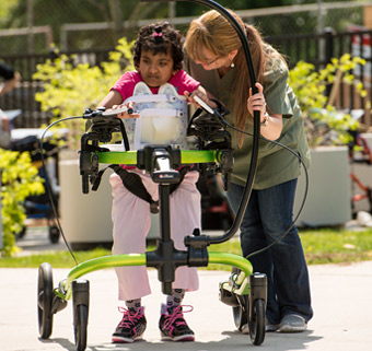 A girl in a green Rifton Pacer with a caretaker