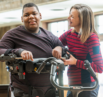 young man using a Rifton TRAM with a caretaker