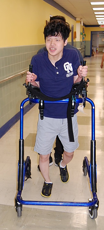 Justin walking down a school hall in a Rifton Pacer gait trainer