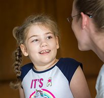 A young girl with braids and a colorful t-shirt smiles at her caregiver.