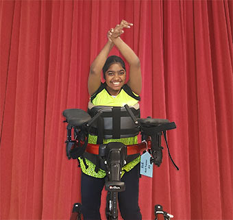 a young girl dancing in a Rifton Pacer gait trainer in front of a red stage curtain