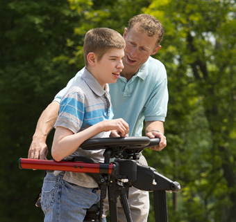A boy walking in a Rifton Pacer gait trainer with the assistance of a caregiver