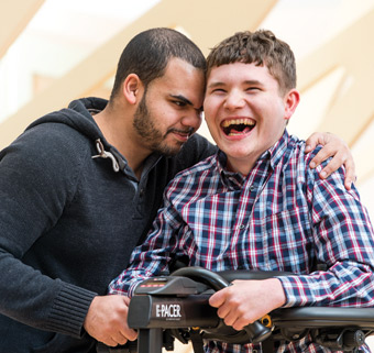 a young man using a Rifton E-Pacer with the assistance of a caretaker