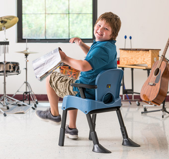 A boy sitting on a Rifton Compass Chair and looking at a book