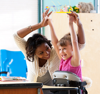 a girl standing in a Rifton Mobile Stander, smiling and holding her hands in the air, with a caretaker