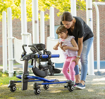 A therapist helps a young girl into a gait trainer