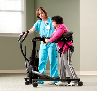 An elderly woman walking in a Rifton TRAM with the assistance of a caretaker