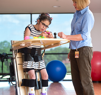 A girl standing in a Rifton Supine Stander, playing a game with her caretaker
