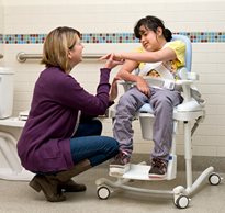 A girl sitting on a Rifton HTS, smiling at her caregiver