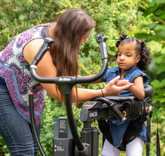 A girl walking in a Rifton E-Pacer, with the help of a therapist