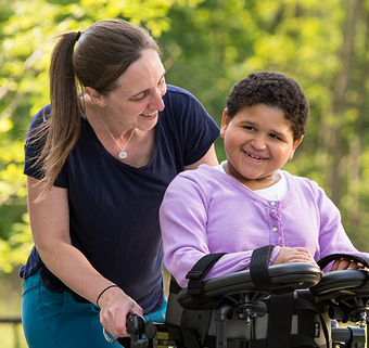 A girl walking in a Rifton Pacer, smiling with her therapist