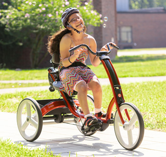 A girl rides on a red Rifton Adaptive Tricycle.