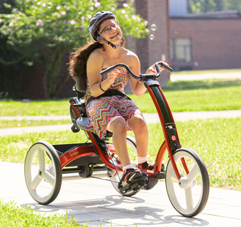 A girl rides on a red Rifton Adaptive Tricycle.