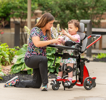 A girl stands in a Rifton Stander and talks with her therapist.