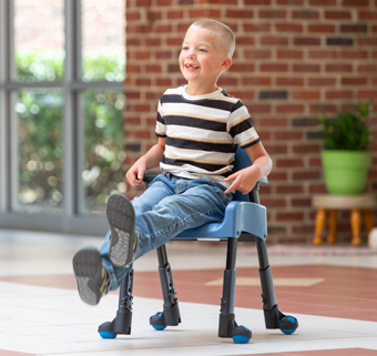 A boy sits in a Rifton Compass Chair and kicks his feet in the air.