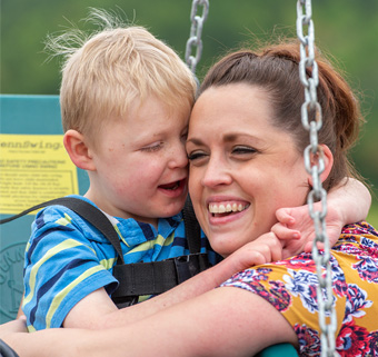 A boy with disabilities sits on a swing and gives his caretaker a hug.