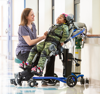 A girl stands in a Rifton Stander and talks with her therapist.