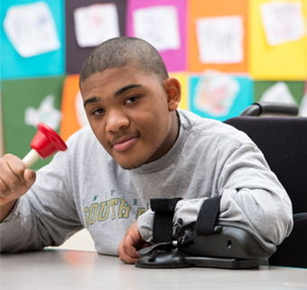 A young man steadies himself with a Rifton Arm Anchor while he rings a bell.