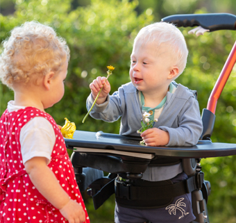 A little boy stands in a Rifton Stander and plays with a little girl.
