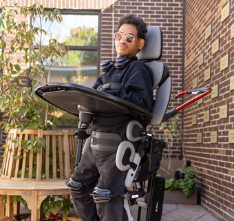 A young man stands in a Rifton Stander and smiles.
