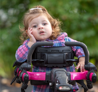 A little girl stands in a Rifton Pacer and smiles.