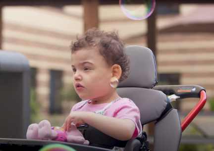 A girl stands in a Rifton Stander and plays with bubbles.