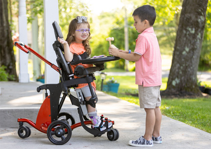 A little girl stands in a Size 1 Rifton Stander and plays with her brother.