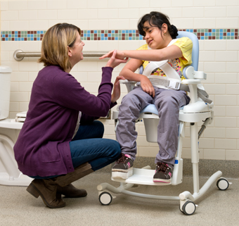 A girl sits in a Rifton HTS and talks with her caretaker.